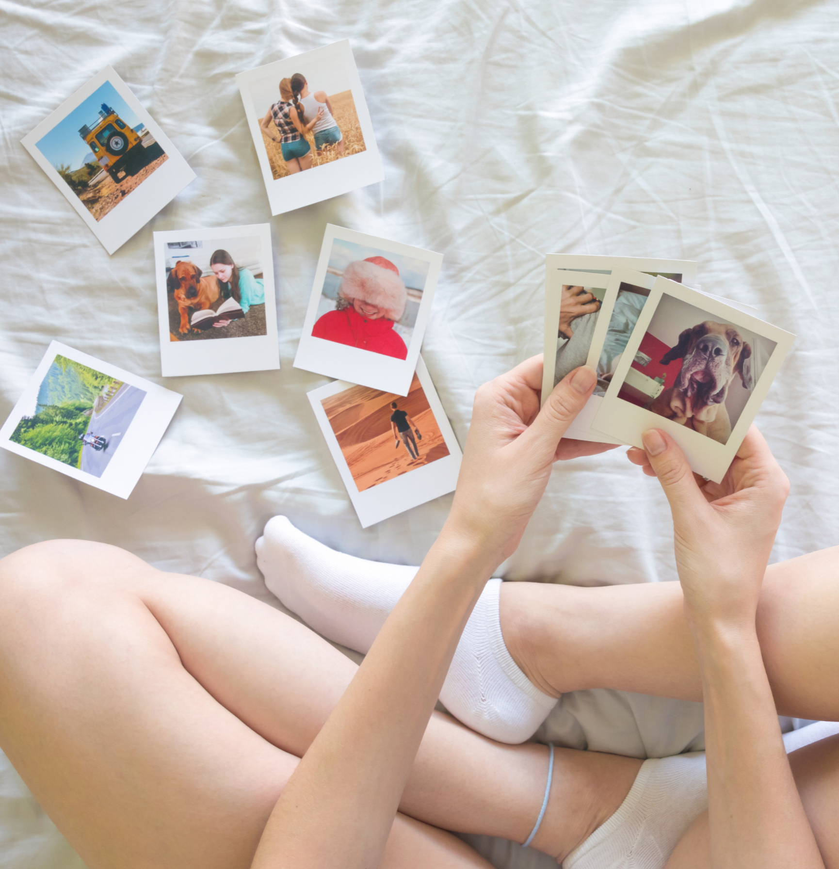 Person holding a photo album with instant photos on a bed